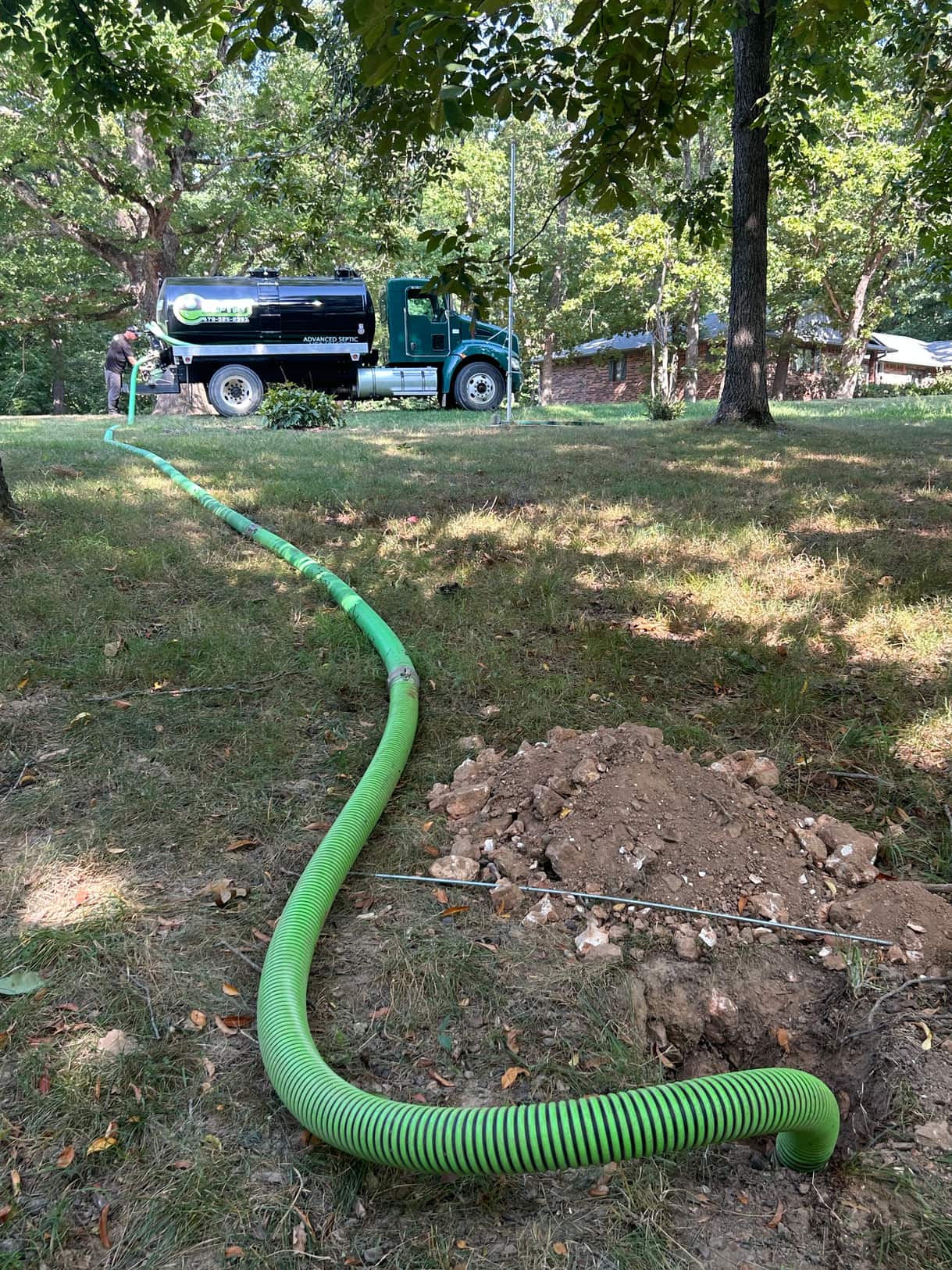 Suction hose running from the Advanced Septic truck across a lawn to an opened septic tank